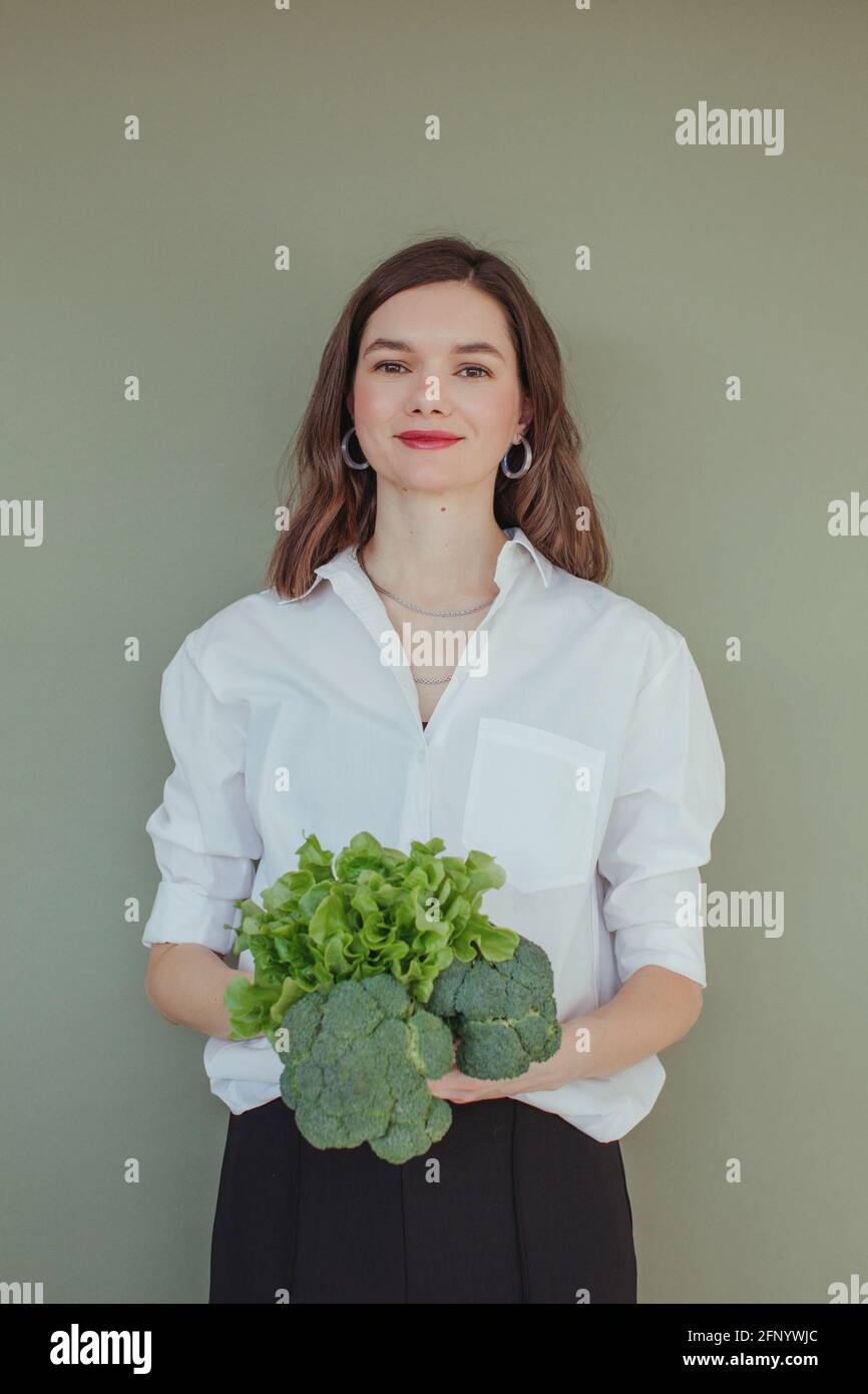 Retrato de una hermosa mujer sonriente sosteniendo brócoli fresco y. lechuga Foto de stock