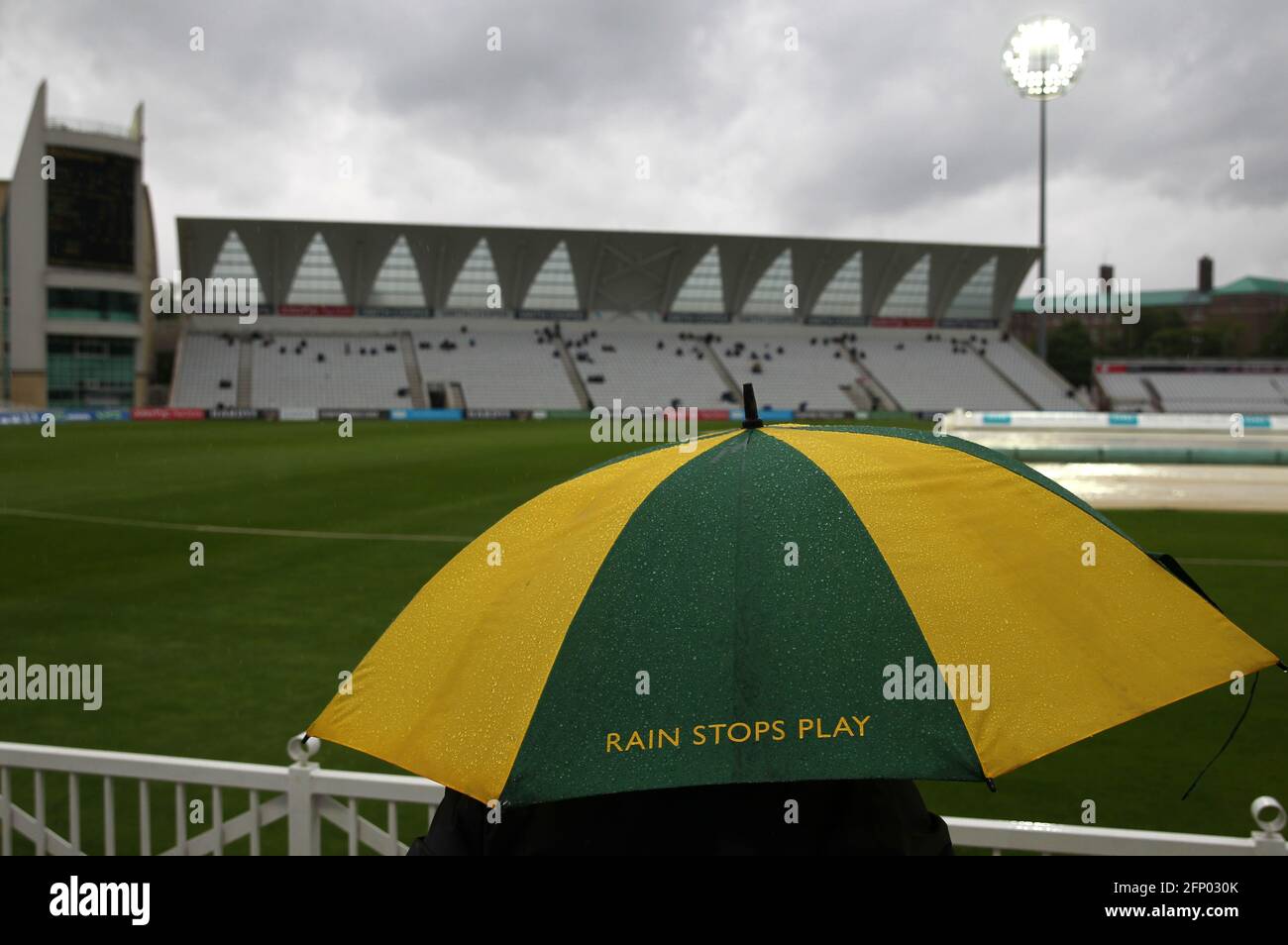 Un espectador se protege bajo una sombrilla de marca Nottinghamshire, ya que las paradas de lluvia juegan durante el primer día del partido del VI = Campeonato del Condado de Seguros en Trent Bridge, Nottingham. Fecha de la foto: Jueves 20 de mayo de 2021. Foto de stock
