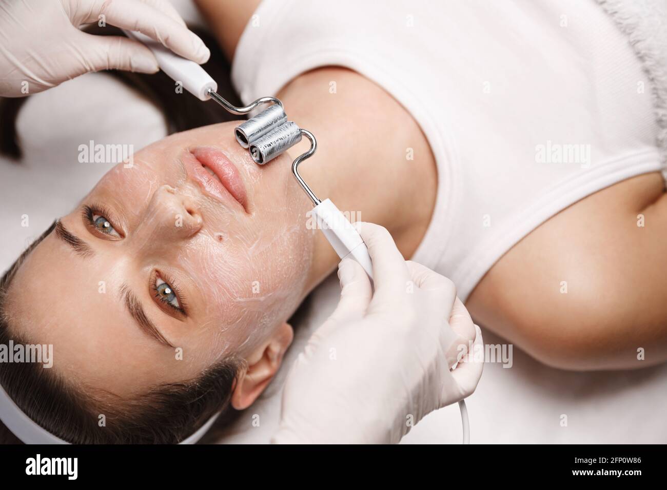 Mujer en la clínica de belleza acostada en la mesa de terapia, esteticista  en guantes utiliza gel galvánico y máquina de electo para aumentar el  oxígeno en las células faciales, rejuvenecer Fotografía