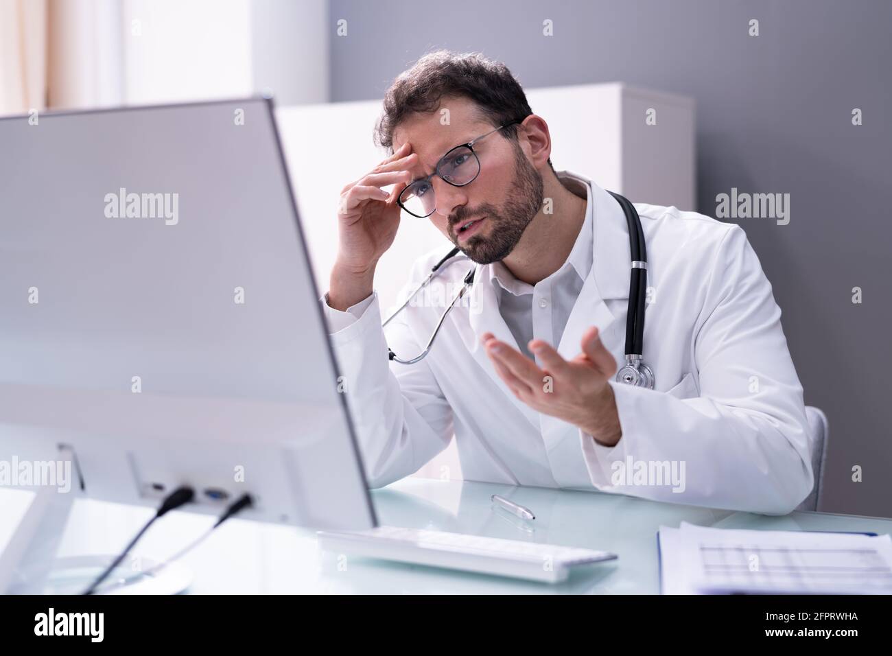 Frustrado doctor en el hospital que trabajaba demasiado mirando la computadora Foto de stock