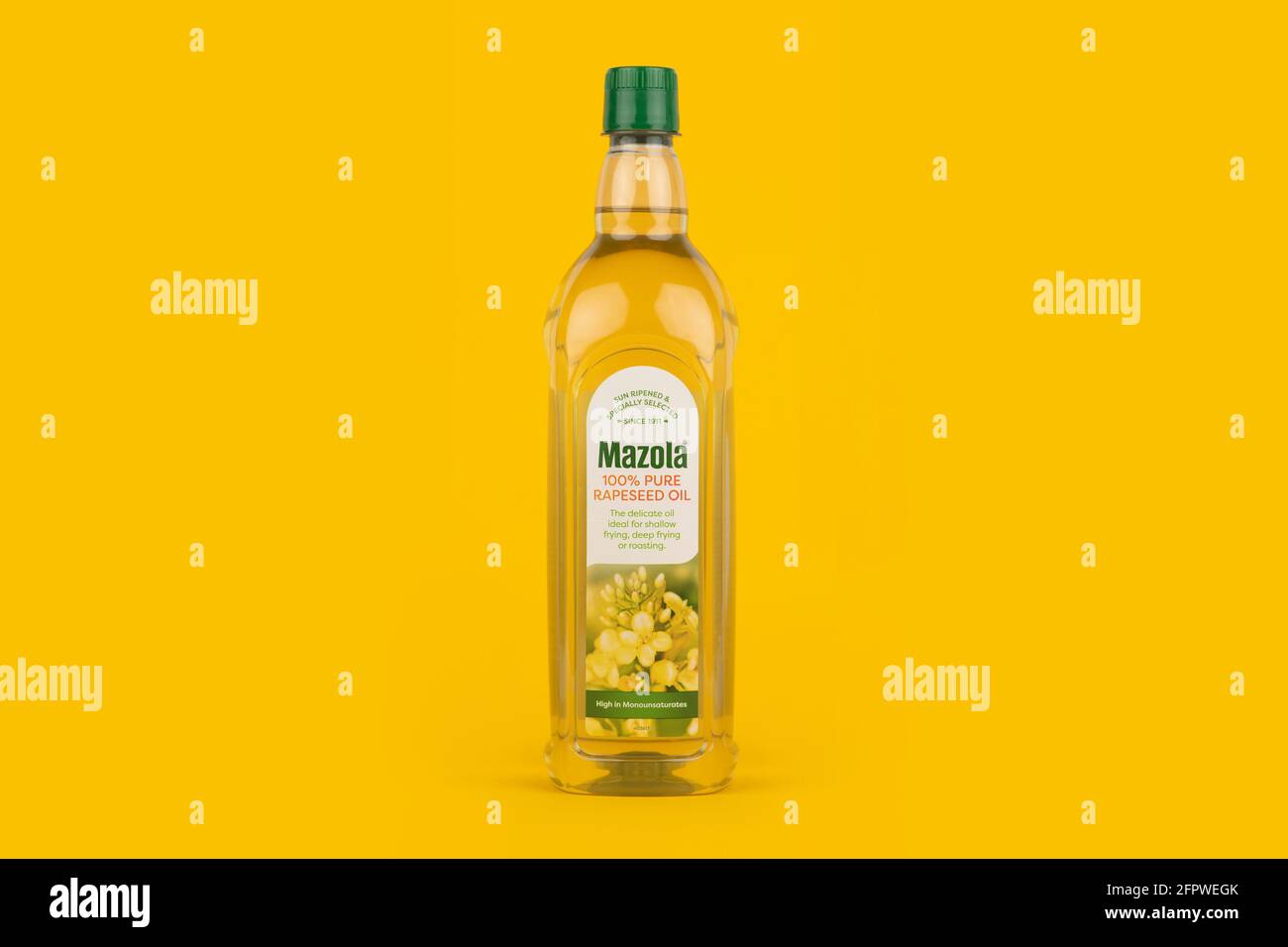 Una botella de Mazola 100 y aceite de colza puro tirado sobre un fondo amarillo. Foto de stock