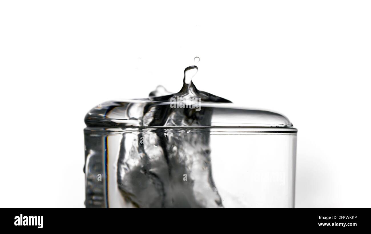 Un pedazo de hielo que cae rápidamente en un cristal transparente y causa  un chapoteo de agua. Ideal para fondos de pantalla para el teléfono o el  ordenador. Lugar para texto, st