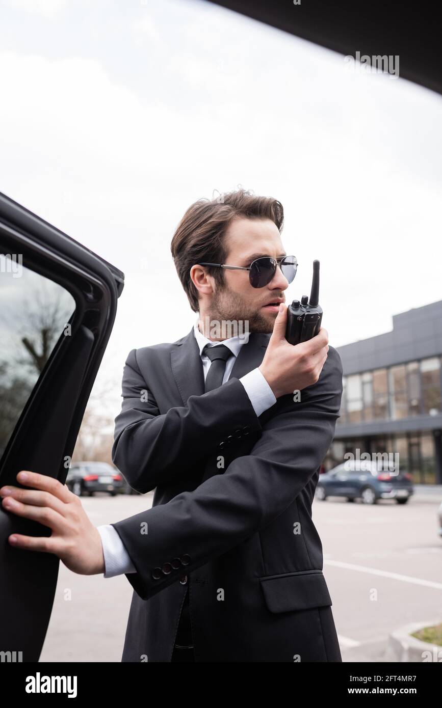 bodyguard con barba en traje y gafas de sol usando walkie talkie
