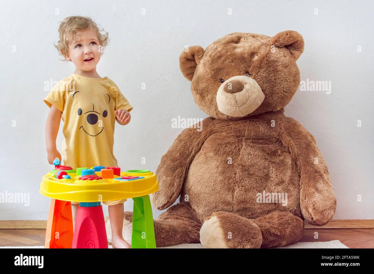 Niño feliz dulce que se divierte jugando en una mesa colorida de  actividades con su oso de peluche gigante, en el interior de casa  Fotografía de stock - Alamy