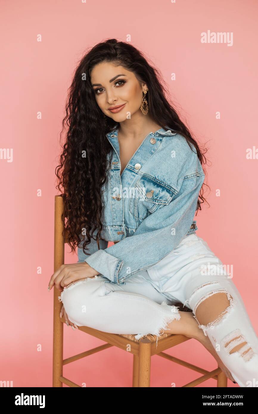 mujer hermosa en chaqueta denim y jeans rasgados se sienta en la silla en  el estudio. belleza y concepto de cuidado personal Fotografía de stock -  Alamy