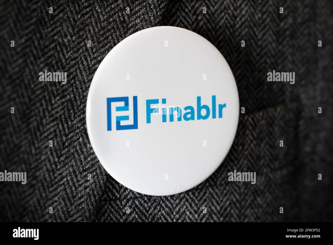 Una insignia de botón con el logotipo de Finablr Financial Services Holding company atada a una chaqueta de traje. Foto de stock