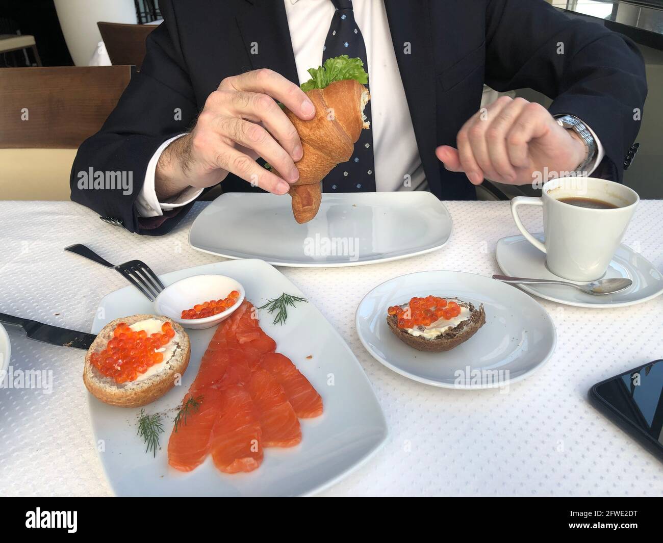 Hombre en un traje de negocios, corbata y camisa blanca es tomar el  desayuno, café, una taza de café, croissant con salmón y ensalada verde,  sándwiches con Fotografía de stock - Alamy