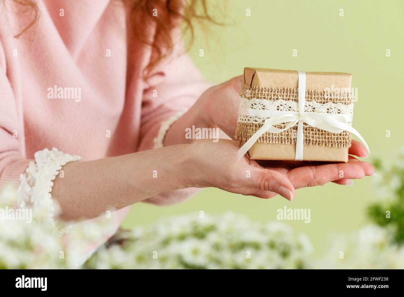 Una mujer joven sostiene, un hermoso envoltorio, regalo. Flores alrededor  de ella. Regalos para ocasiones especiales Fotografía de stock - Alamy