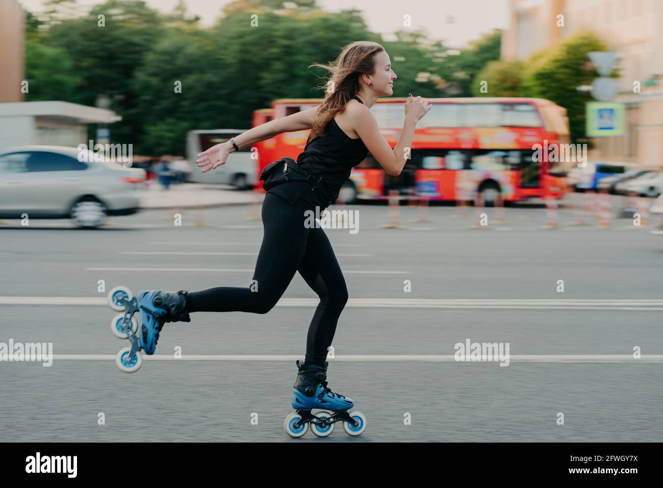 Mujer en patines de con ruedas durante el día de verano en una carretera ajetreada con el transporte lleva el estilo de vida activo se viste negro ropa deportiva Fotografía