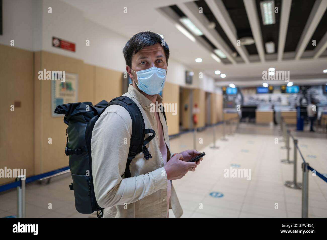 Reglas de vuelo durante la pandemia de Covid-19 sólo en mascarilla  protectora. Nuevo concepto normal. Hombre enmascarado con el teléfono en la  mano y la mochila de pie en línea a Fotografía