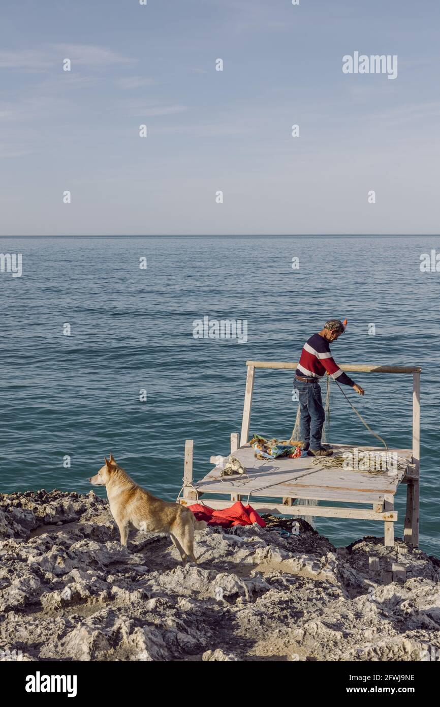Viejos pescadores con su perro en Apulia sobre una roca Acantilado en el sur de Italia Foto de stock