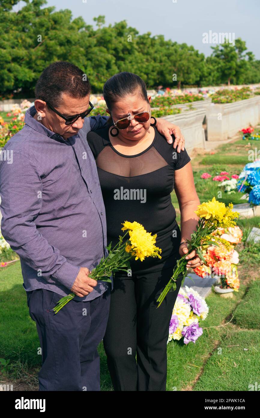 Centímetro Sinfonía salto Luto pareja mayor sosteniendo flores en las manos y de pie en la tumba en  el cementerio Fotografía de stock - Alamy