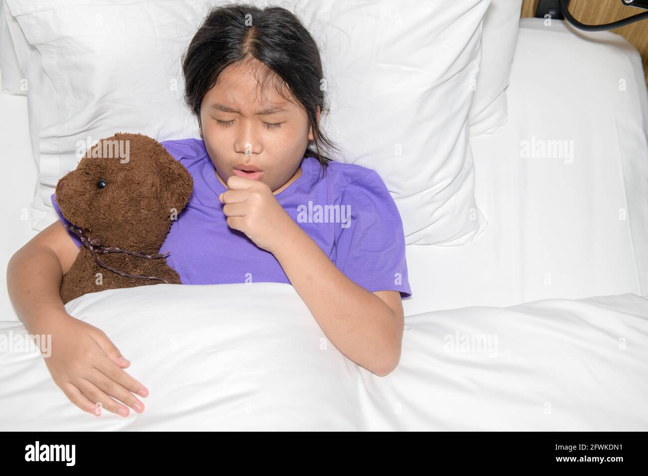 La niña tiene tos y dolor de garganta debido a estar enferma debido a COVID  19 o gripe y acostada con un juguete de oso en la cama, un conpet de  atención