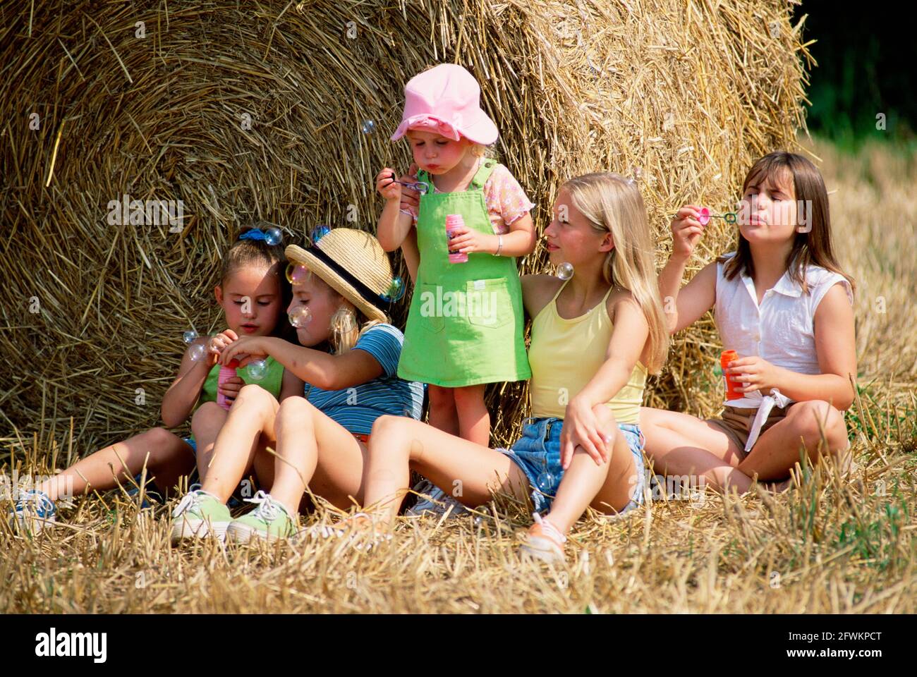 Estilo de vida. Niños. Cinco niñas al aire libre por fardos de heno enrollados en la granja. Foto de stock