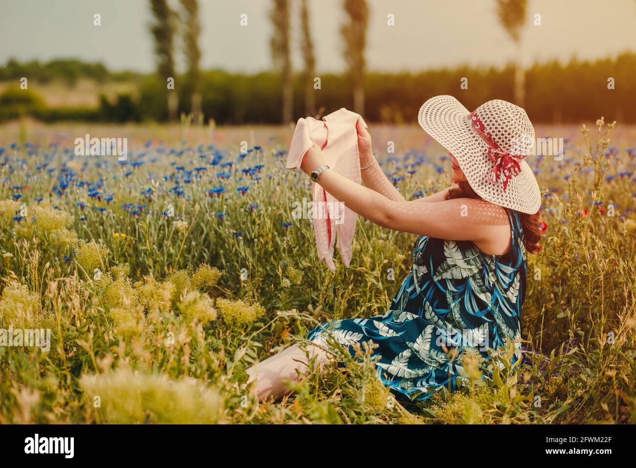 Joven mujer disfrutando su maternidad, sentada en el campo llena de flores coloridas y sosteniendo su ropa bebé Fotografía de stock - Alamy