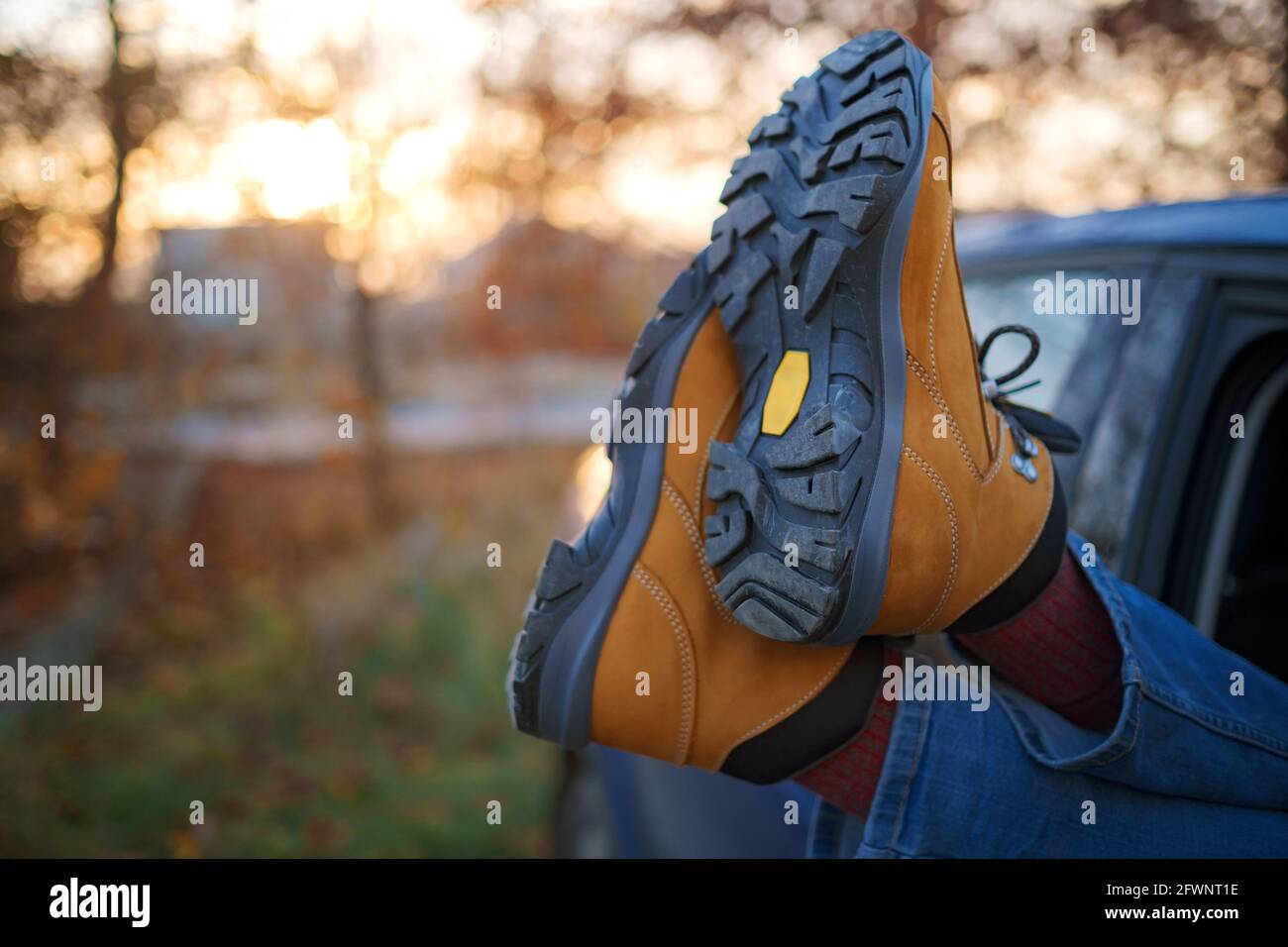 Mujer pies en las botas de senderismo de moda amarillo en la puerta del  coche. Pies fuera de la ventana al bosque al atardecer. El concepto de  libertad de circulación. Un fin