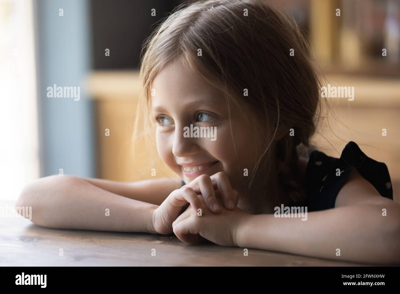 Feliz linda chica pre adolescente sentada en la mesa de la cocina Foto de stock