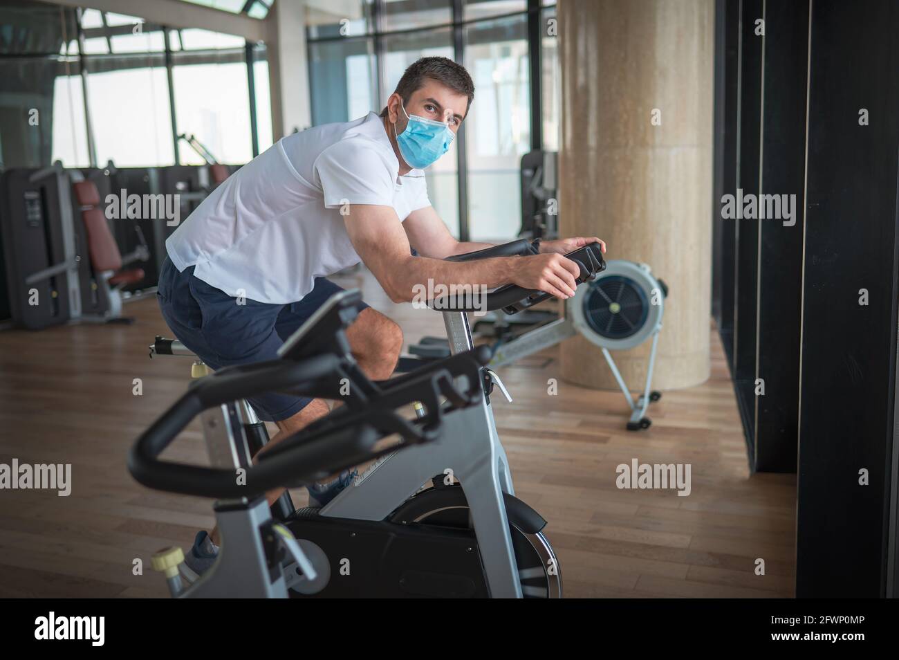 Hombre caucásico haciendo ejercicio en el gimnasio montando bicicleta estática en bicicleta interior. Estilo de vida saludable con Covid-19 resumen de prevención del coronavirus Foto de stock