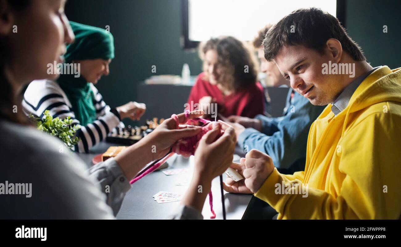 Grupo de personas jugando a las cartas y a los juegos de mesa en el centro comunitario, inclusividad de una persona discapacitada. Foto de stock