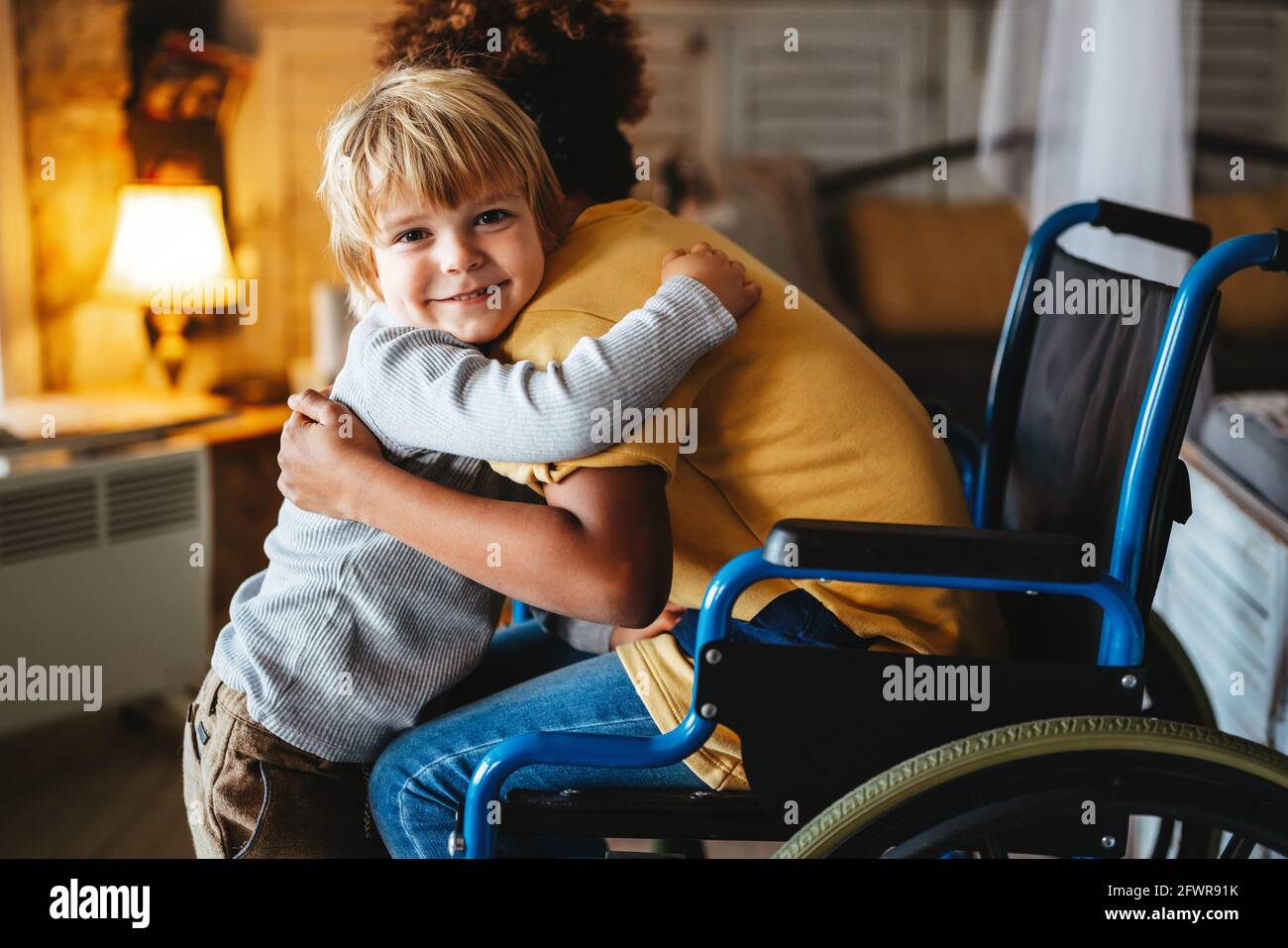 Niña negra con discapacidad en silla de ruedas abrazada con su hermano menor. Foto de stock