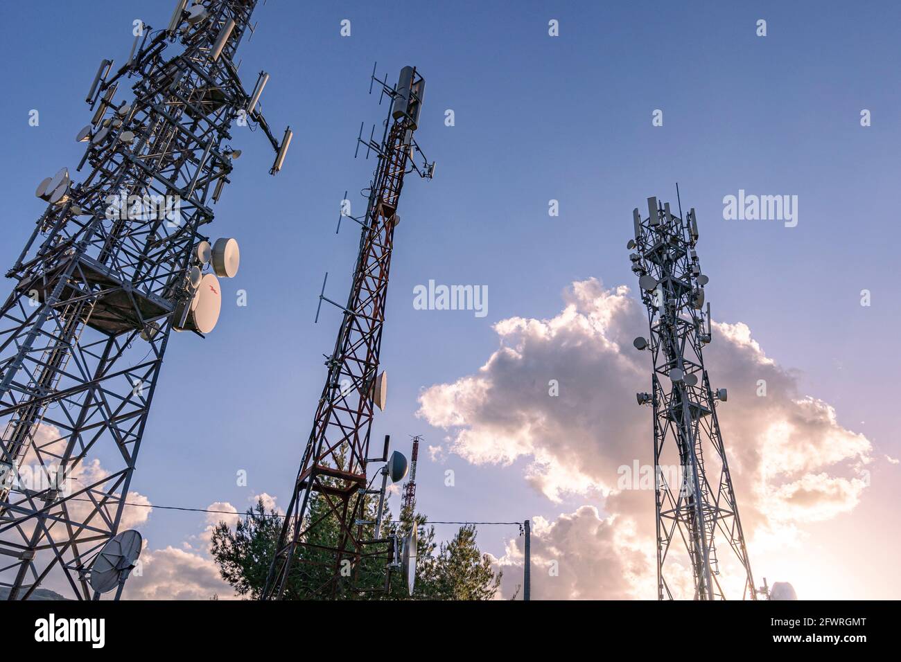 Tres antenas de comunicación por satélite, celular o televisión se destacan en el cielo con una nube iluminada por el sol que se pone. Abruzzo, Italia, Europ Foto de stock