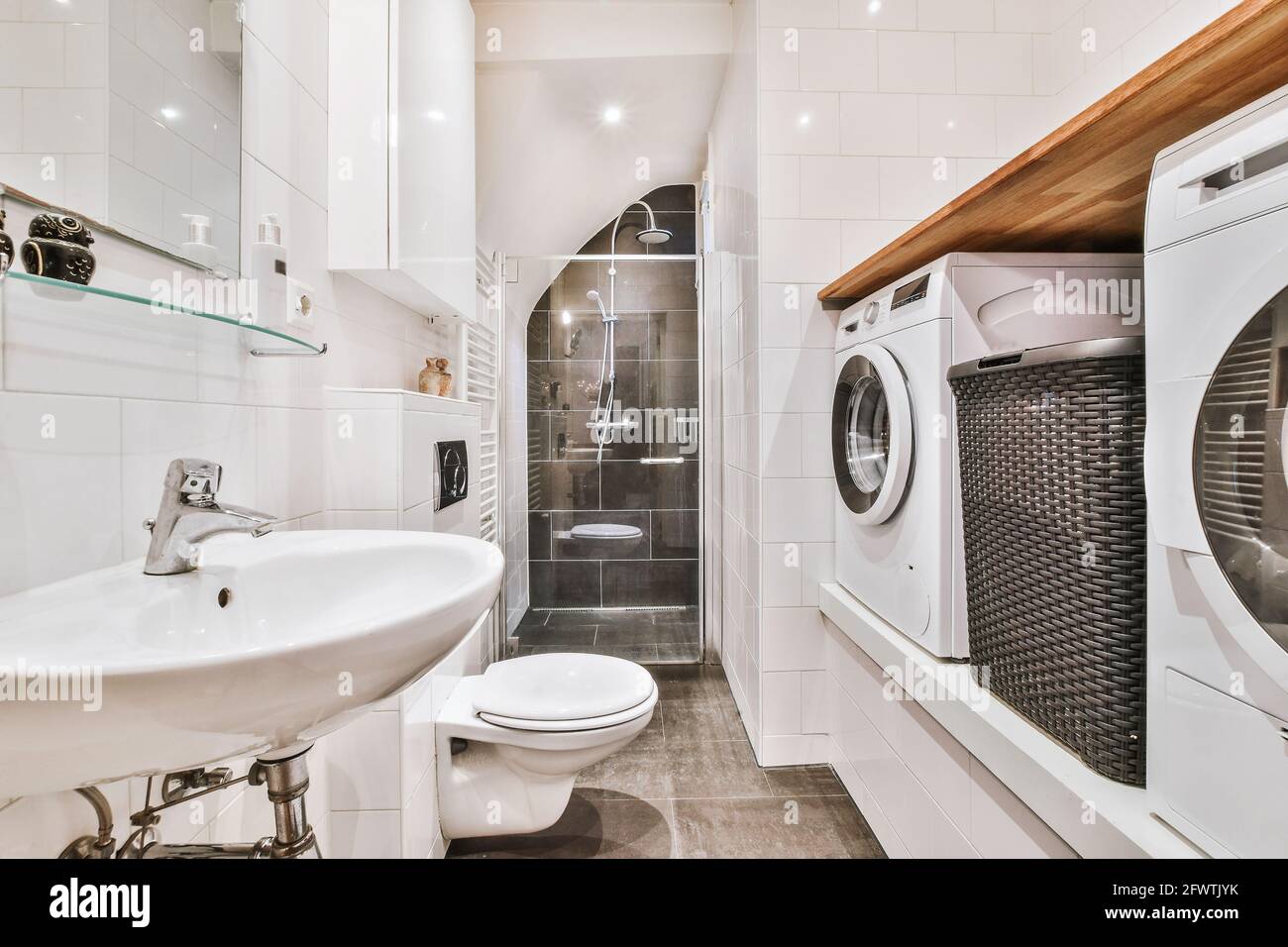 Un cuarto de lavado con azulejos blancos en las paredes y estantes de  madera frente a la lavadora secadora y secadora.