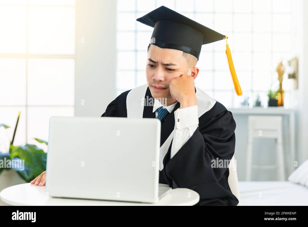graduación masculina frustrada tratando de aprender en línea en casa Foto de stock