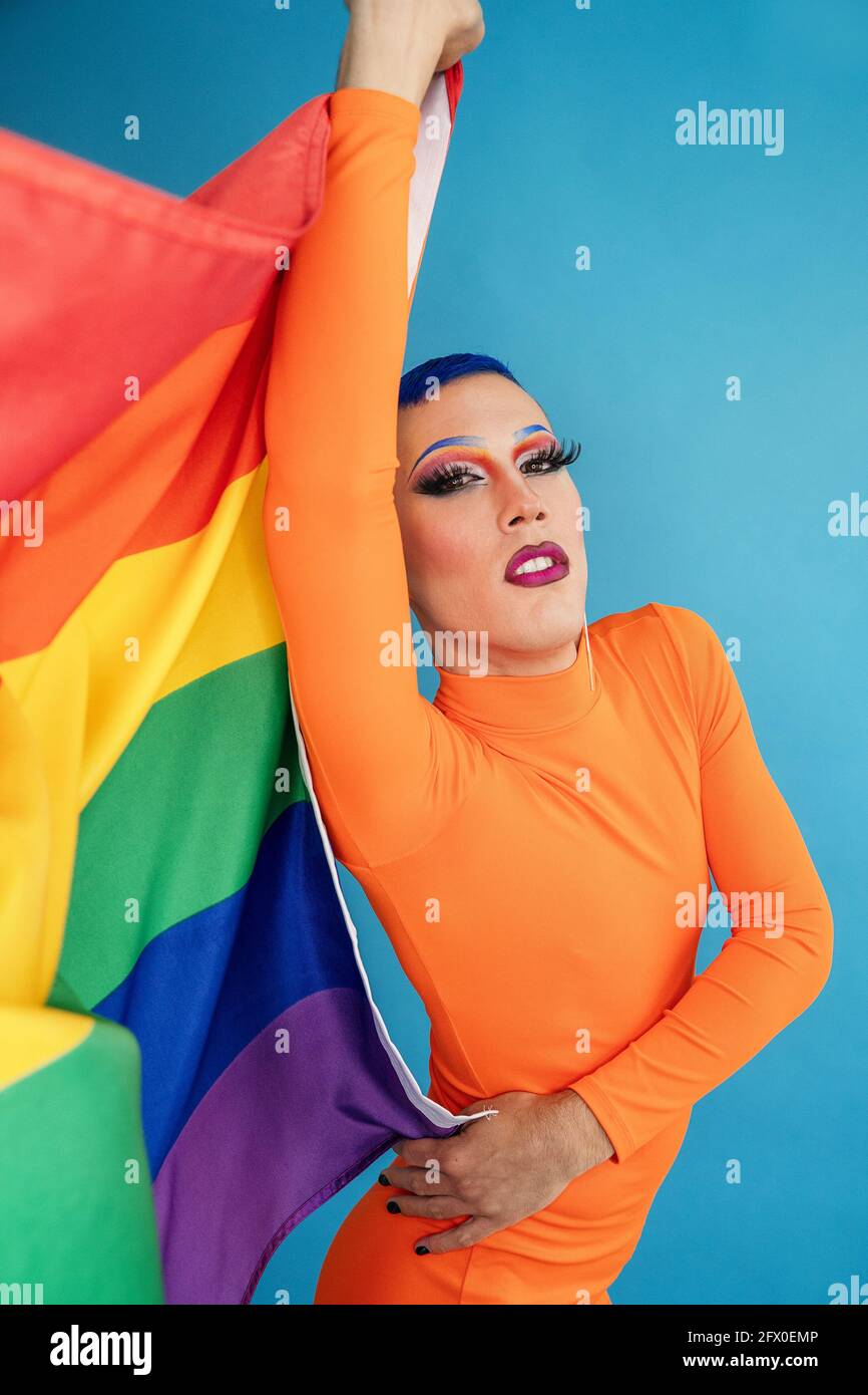 Delgada y extraordinaria reina de arrastre con maquillaje provocativo que  mantiene el orgullo LGBT bandera contra fondo azul y mirando la cámara  Fotografía de stock - Alamy