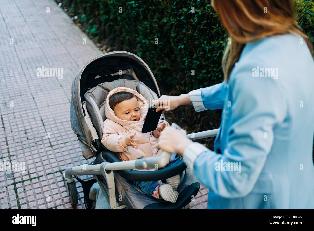 Desde arriba lindo bebé divertido con smartphone con ropa de abrigo sentado  en el cochecito y mirando a la mamá borrosa en primavera calle Fotografía  de stock - Alamy