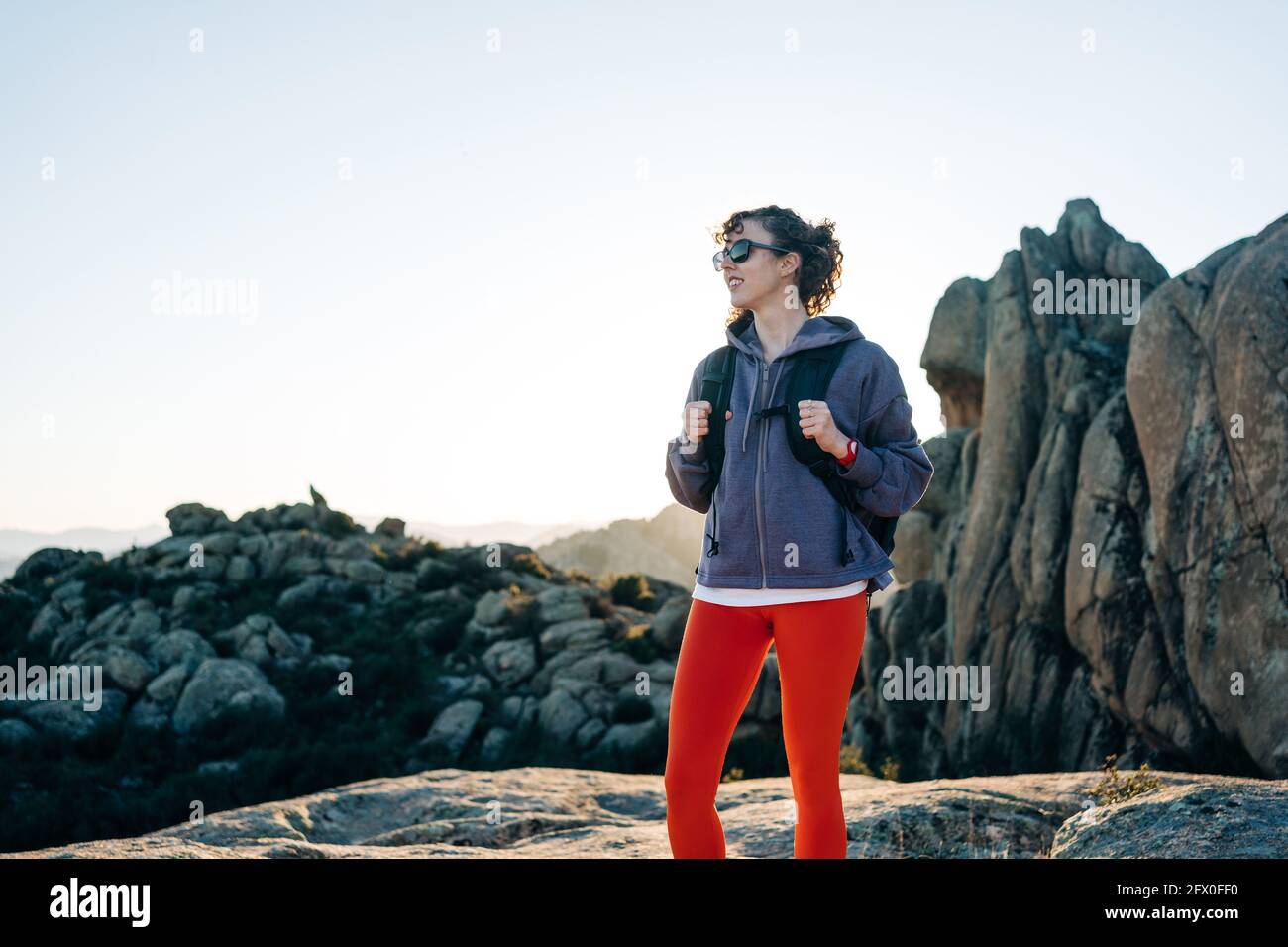 Alegre joven mujer explorador en sudadera con capucha y gafas de sol  sonriendo mientras admirando la naturaleza durante el senderismo en el  valle montañoso rocoso soleado día Fotografía de stock - Alamy