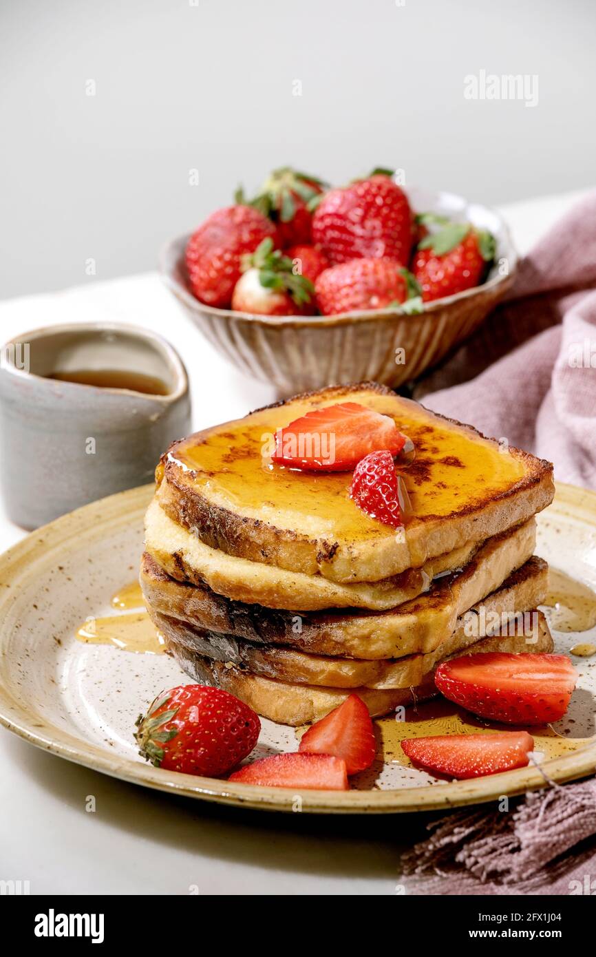 Reserva de tostadas francesas con fresas frescas en placa de cerámica, jarabe de arce en jarra de cerámica y servilleta de tela rosa sobre mesa blanca. Desayuno casero Foto de stock