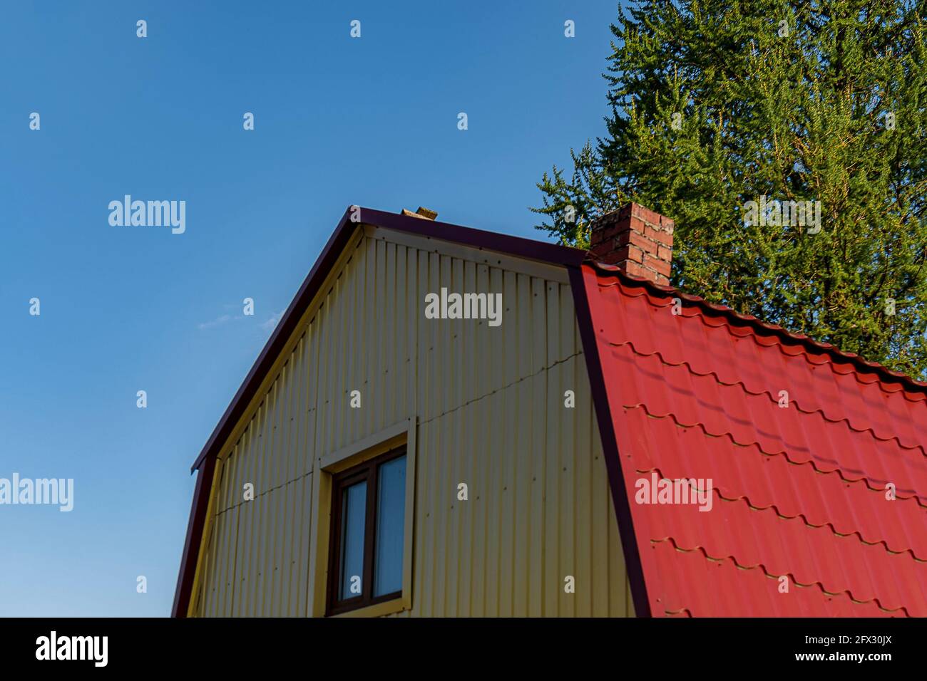 El techo rojo del ático está hecho de metal de la casa con una ventana. Al aire libre del día. Vista posterior. Foto de stock