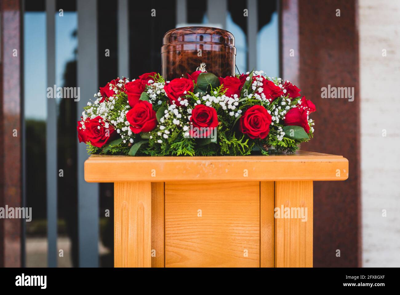 Urna funeraria con cenizas de muertos y flores en funeral. Urna de entierro  decorada con flores en el servicio conmemorativo en un stand de madera,  triste y penoso último Fotografía de stock -