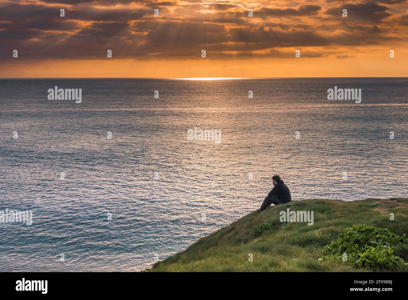 Un hombre sentado en Towan Head disfrutando de una espectacular puesta de sol sobre Fistral Bay en Newquay en Cornwall. Foto de stock