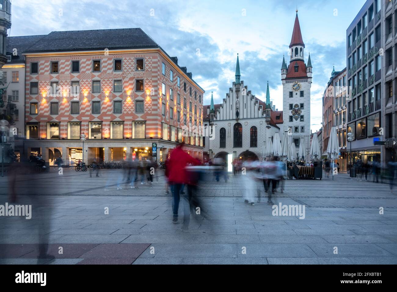 Gente incidental caminando por el sendero durante el anochecer en Marienplatz con el Antiguo Ayuntamiento de Munich, Baviera, Alemania Foto de stock