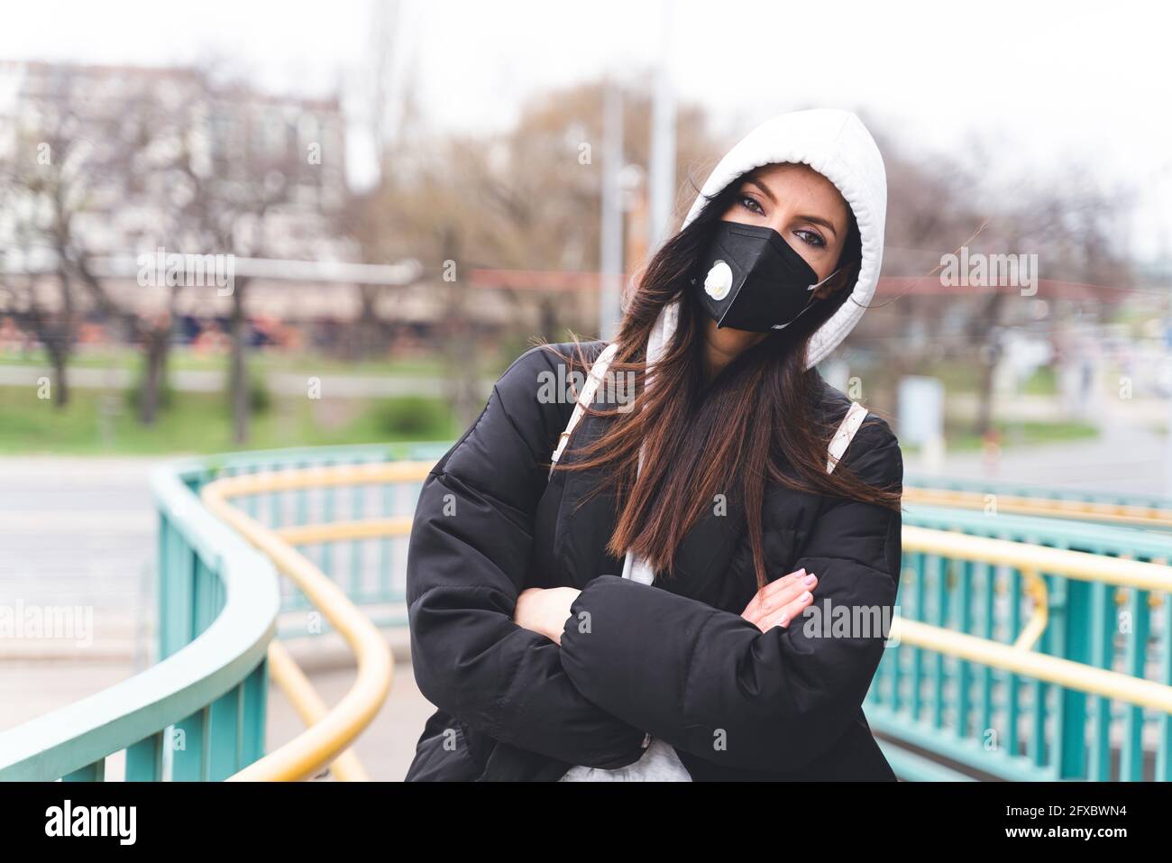 Mujer con máscara facial y chaqueta con capucha mirando fijamente mientras  está de pie con los brazos cruzados Fotografía de stock - Alamy