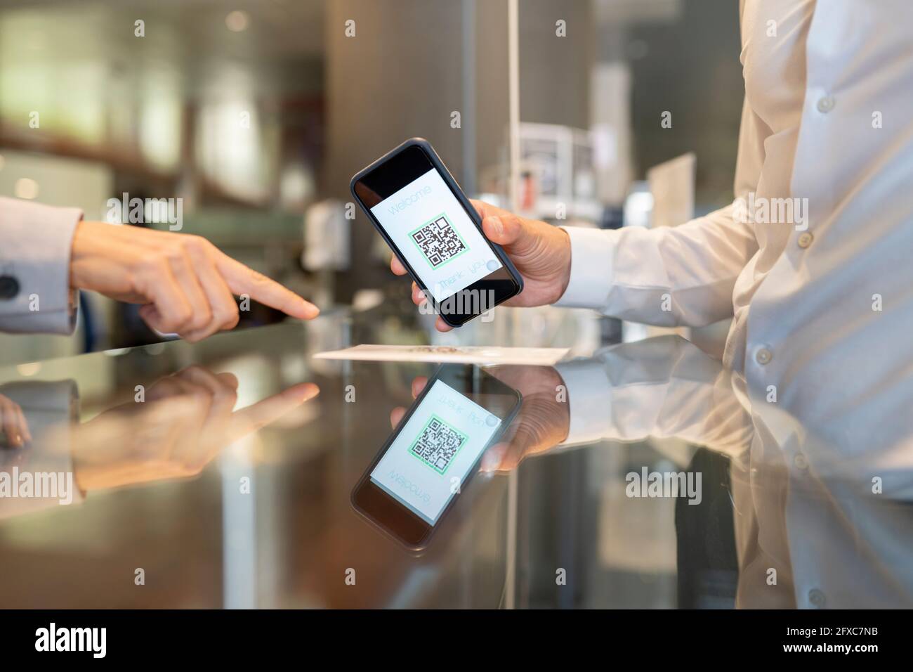 Recepcionista mujer señalando el código QR escaneado por cliente masculino en el escritorio Foto de stock