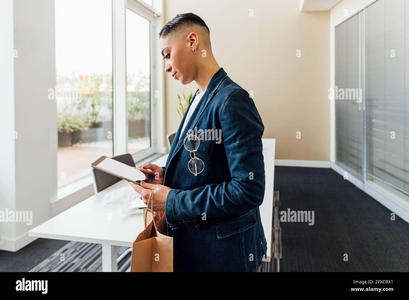 Joven emprendedor con bolsa de papel usando tablet digital en la oficina Foto de stock