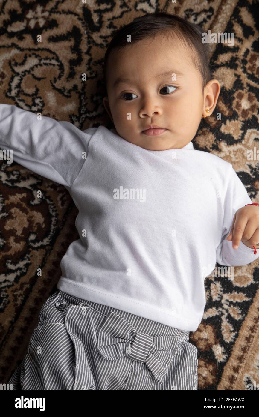 primer plano de un bebé hermoso y adorable tumbado en una alfombra  texturizada, llevando pantalones cortos y un pelele blanco, bebé en el  estudio Fotografía de stock - Alamy