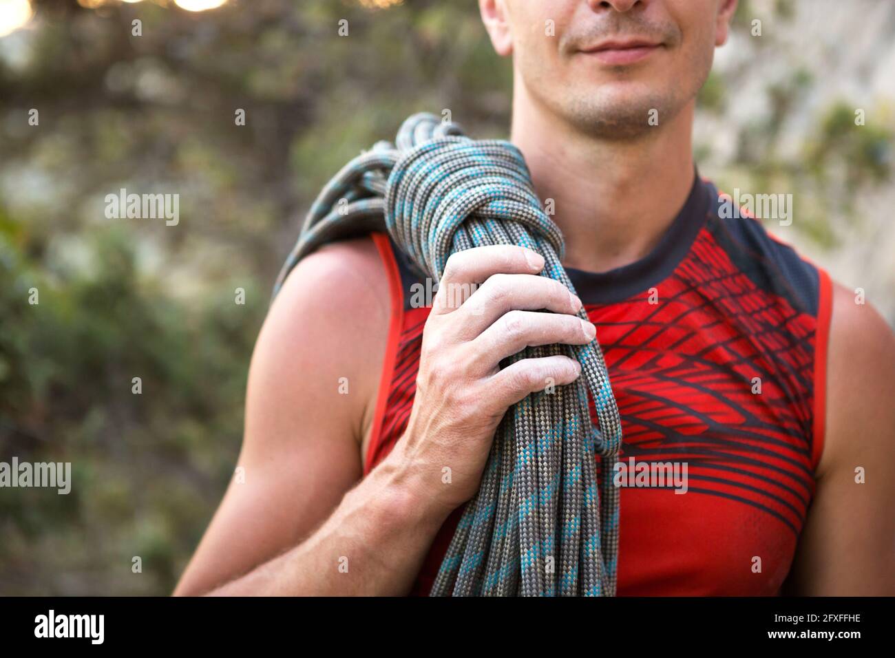 Un escalador masculino de aspecto caucásico con una cuerda enrollada en su mano. Cuerda de cuerda, nudo, almacenamiento de equipo. Mano en magnesia blanca. Rojo deportes Jerse Foto de stock