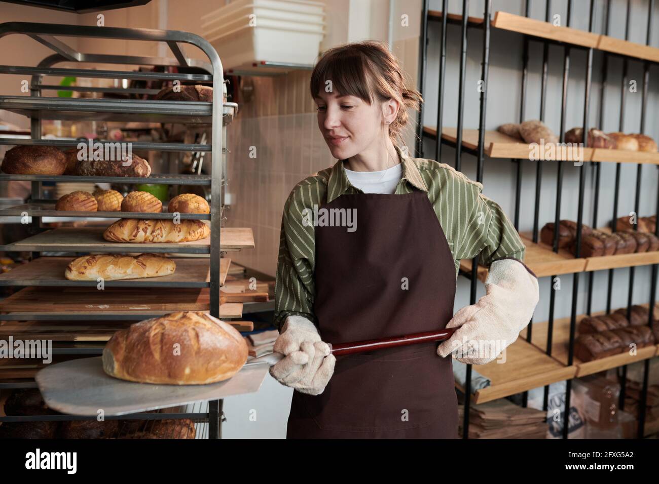 Mujer joven en uniforme horneando pan fresco en el horno en la panadería  Fotografía de stock - Alamy