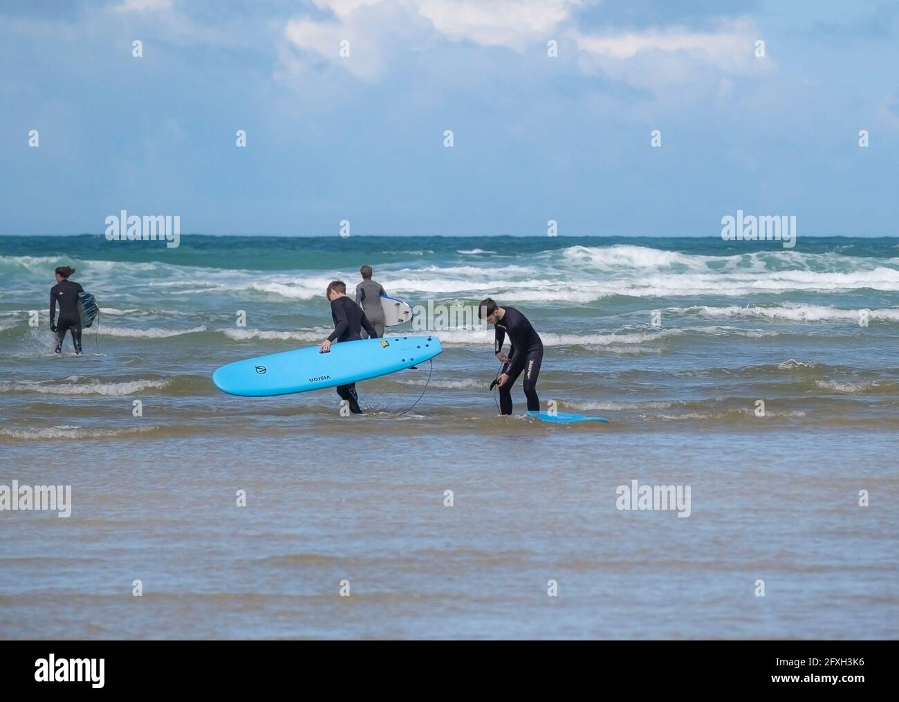 Un grupo de jóvenes amigos masculinos llevando sus tablas de surf contratadas Caminando en el mar en Mawgan Porth para comenzar un Sesión de surf en una estaycation de Cornualles Foto de stock