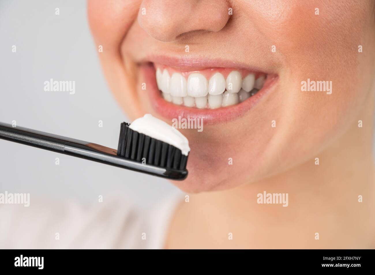 Una mujer con una sonrisa blanca como la nieve sostiene un cepillo de dientes con pegar sobre un fondo blanco Foto de stock
