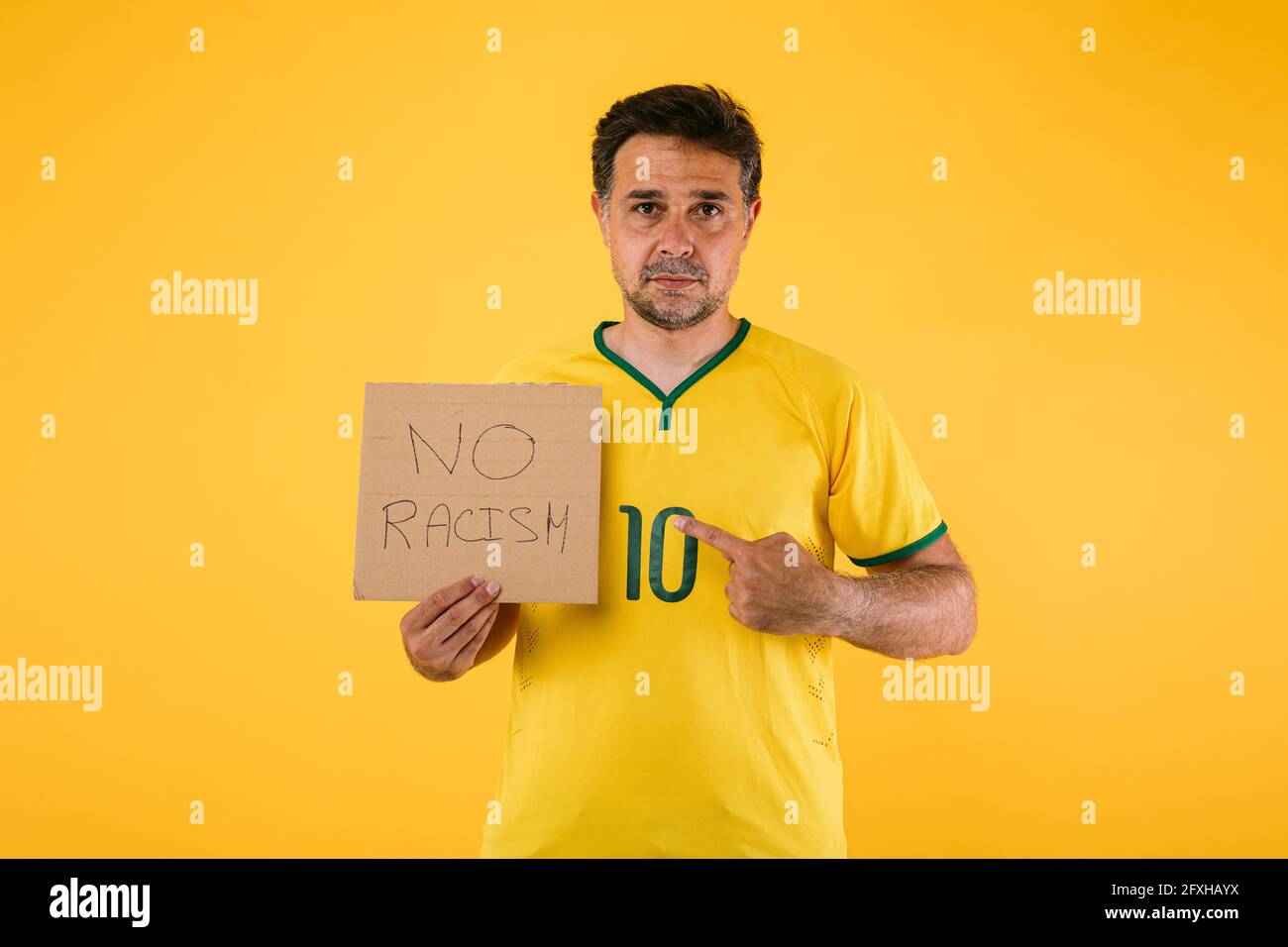 Un fan de fútbol brasileño con camiseta amarilla y un signo de eso Dice 'No racismo' Foto de stock