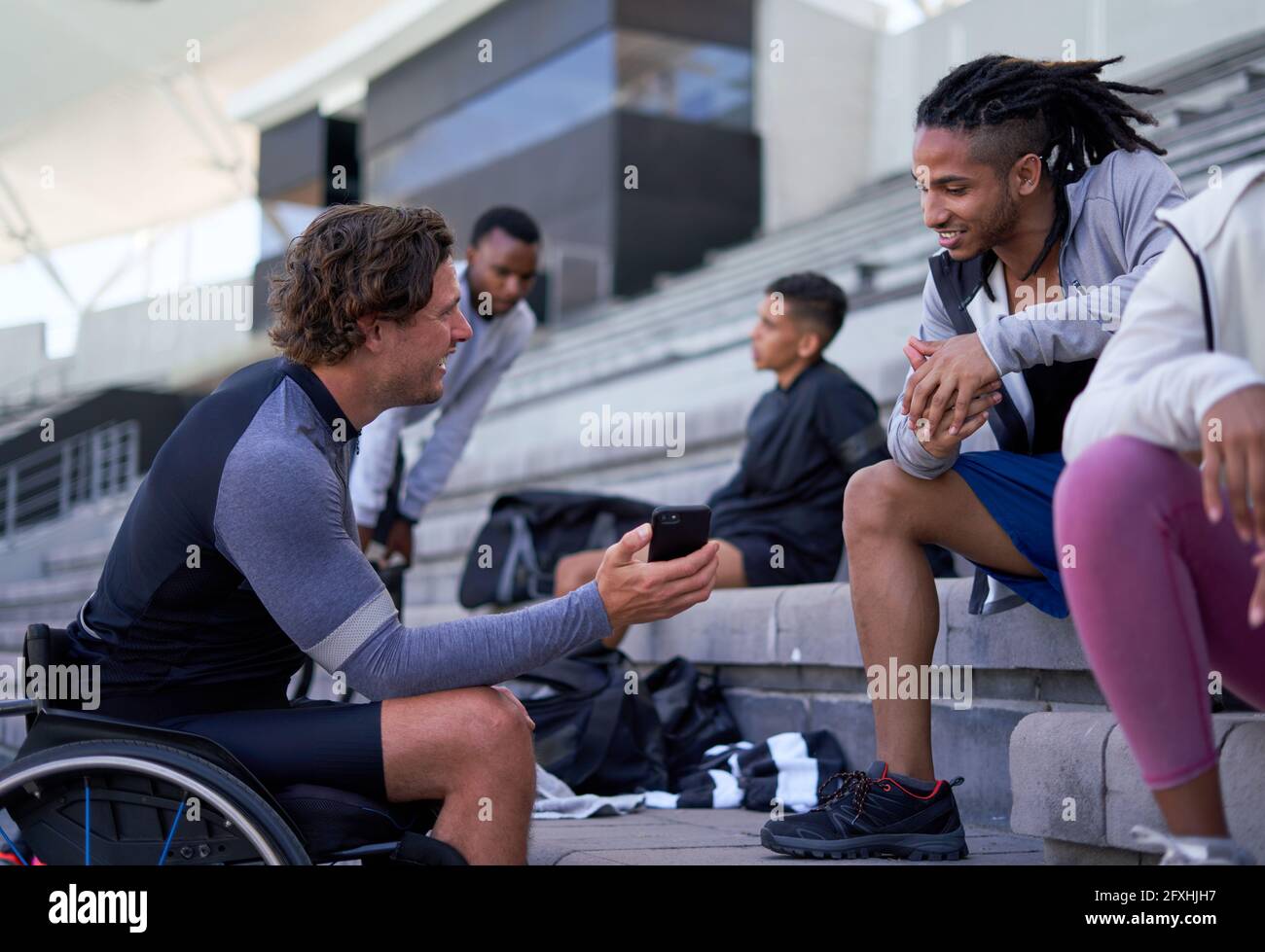 Atleta en silla de ruedas mostrando el teléfono inteligente a un amigo en los gradas del estadio Foto de stock