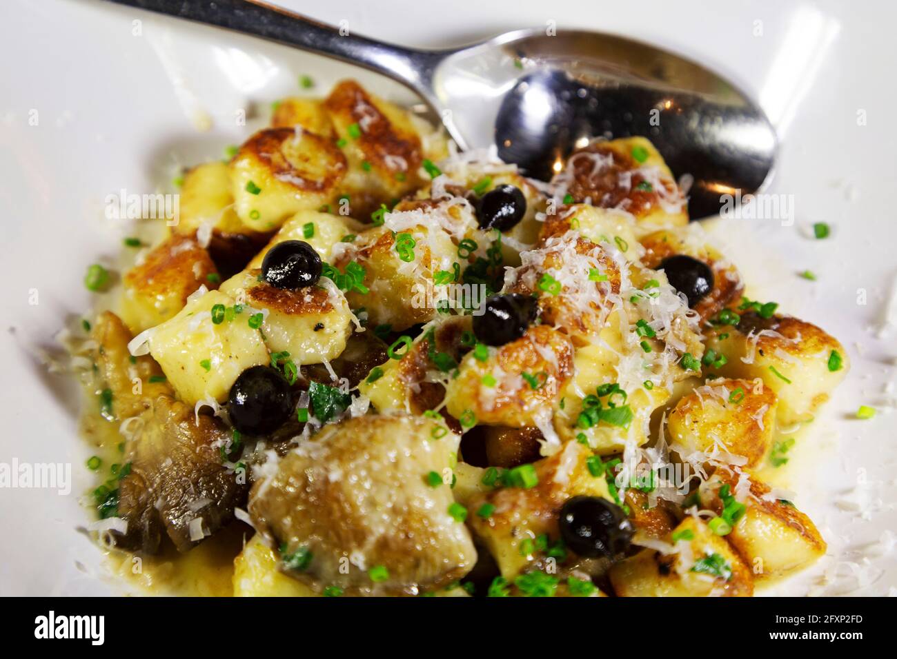 Gnocchi cocido con aceitunas y queso parmesano rallado. El plato está regado con aceite de oliva. Foto de stock