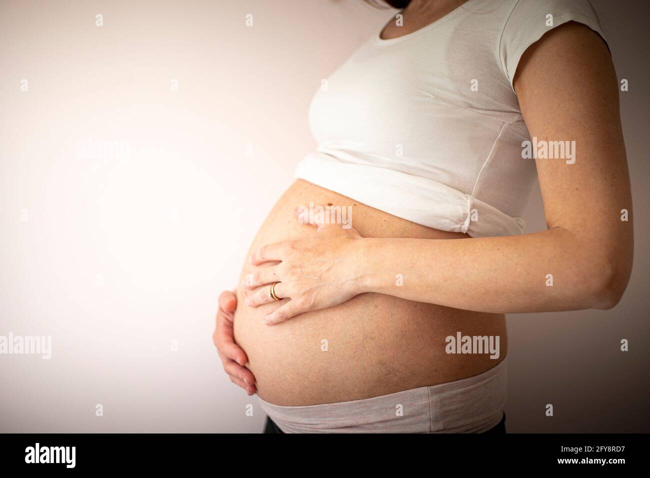 Mujer embarazada con una camiseta blanca con las manos en el vientre sobre fondo en blanco. Perfil, vista lateral. Fondo con espacio de copia. Foto de stock