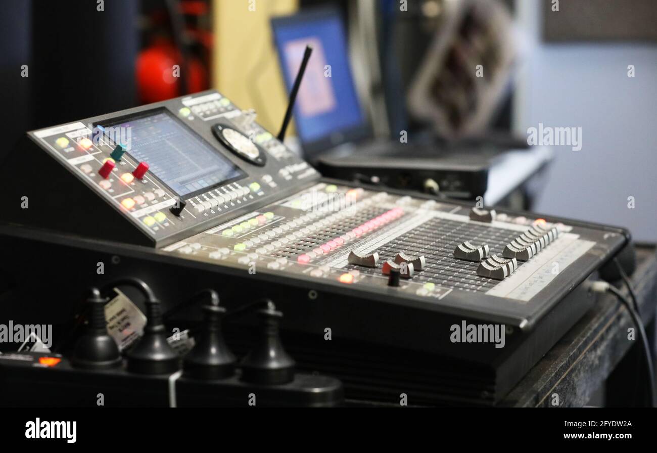 Un pequeño estudio de ingeniería de sonido con plataforma o tabla de mezclas y un ordenador portátil en el fondo. Placa con varias luces, interruptores, diales y mandos de nivel Foto de stock