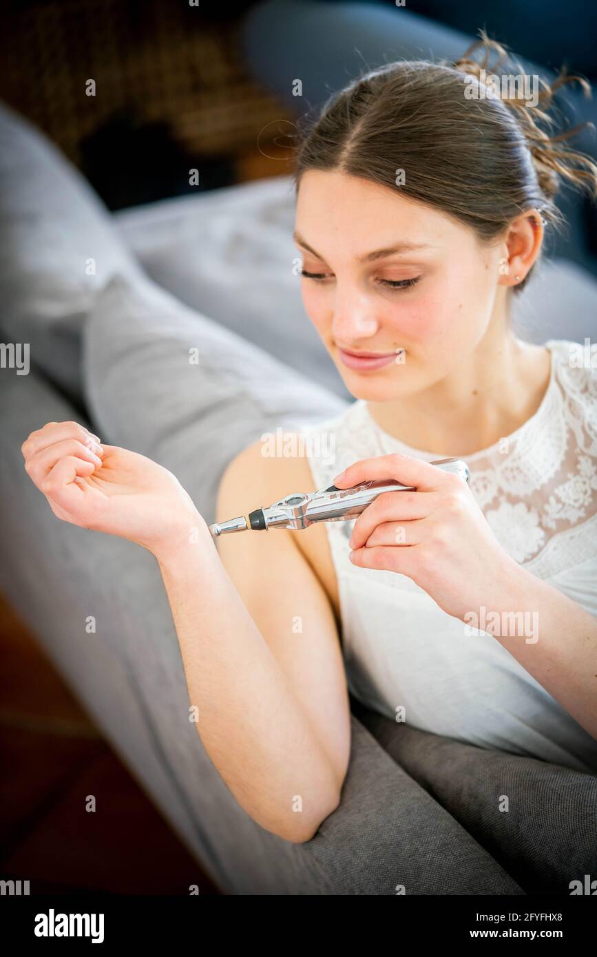 Mujer que usa un bolígrafo electrónico de acupuntura masajeador de meridianos de energía para aliviar el dolor. Foto de stock