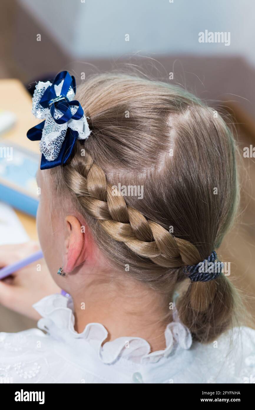 Primer plano del peinado de una chica con una trenza alrededor de su cabeza  y un arco azul. El peinado se hace con horquillas y una banda elástica.  Sólo la parte posterior